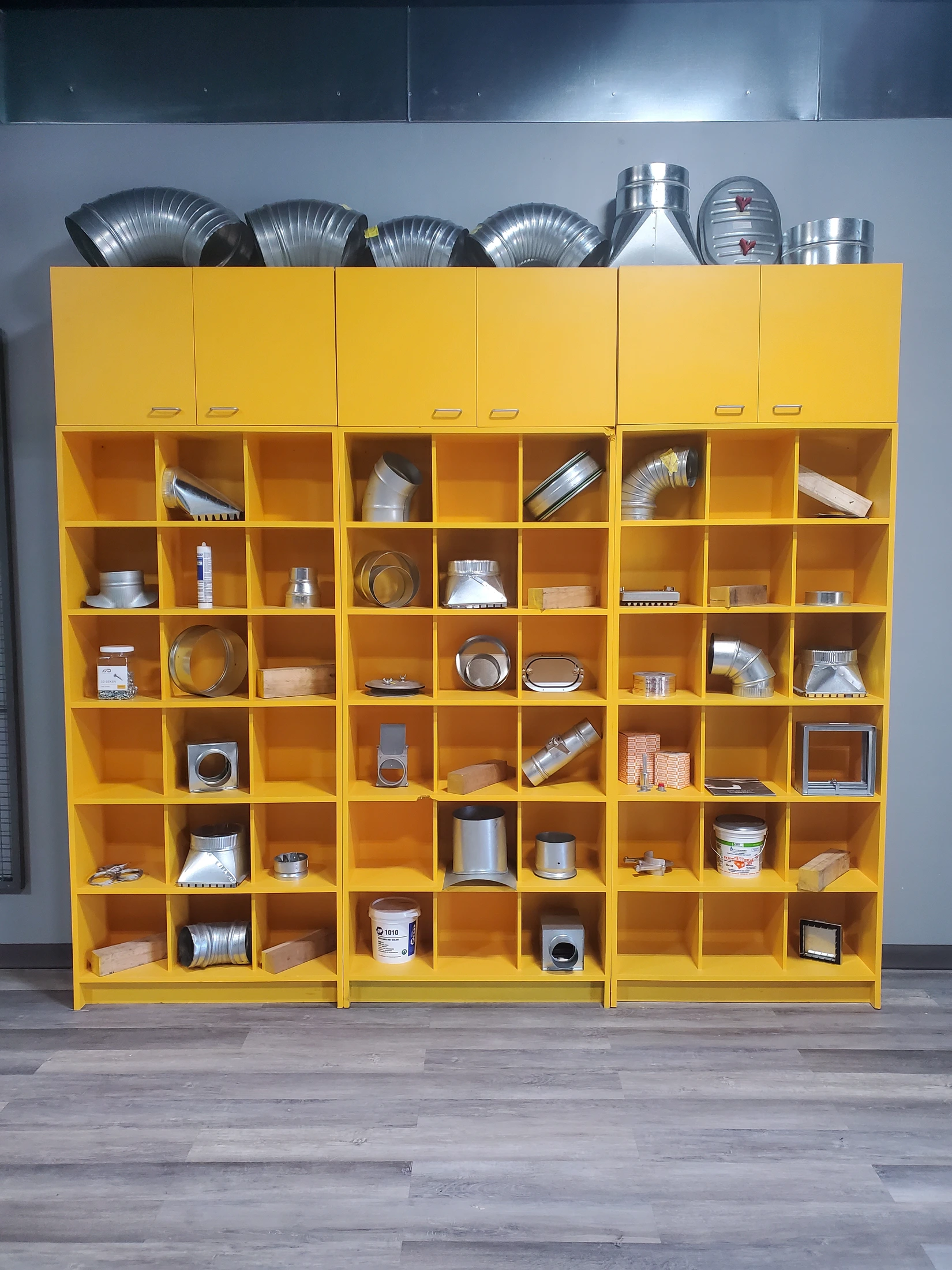 Yellow in-store display cabinets arranged with duct fittings, connectors, access doors, and other HVAC products