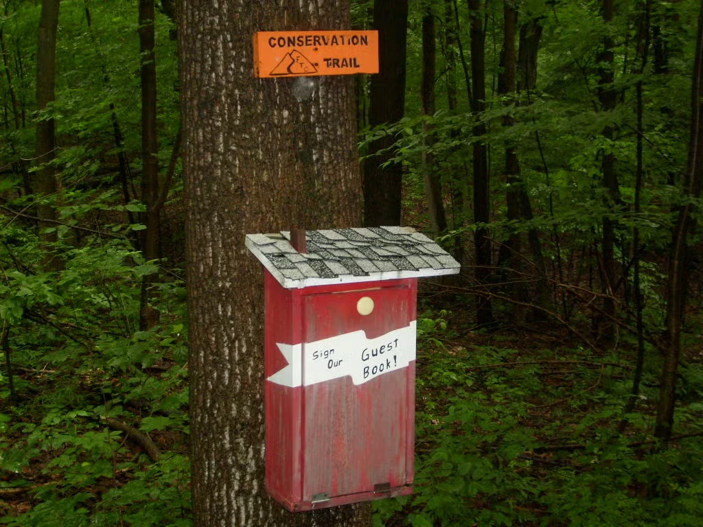 A red guestbook box attached to a tree beneath a Conservation Trail sign
