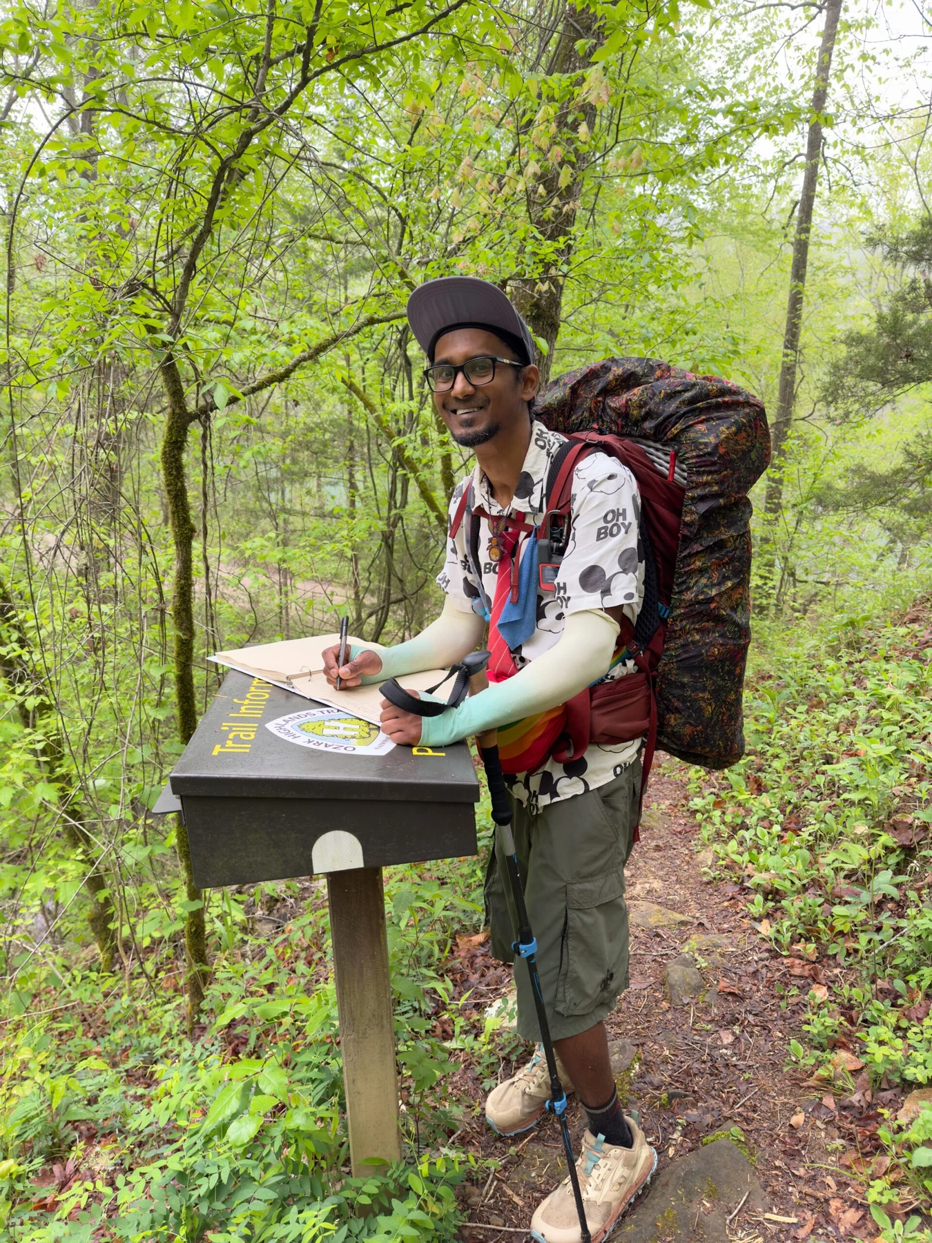 A backpacker wearing glasses signing a trail register at a forest information box
